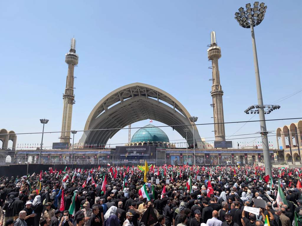 Mourners gather at the Grand Mosalla in Tehran holding red flags for Ayatollah Khamenei.
